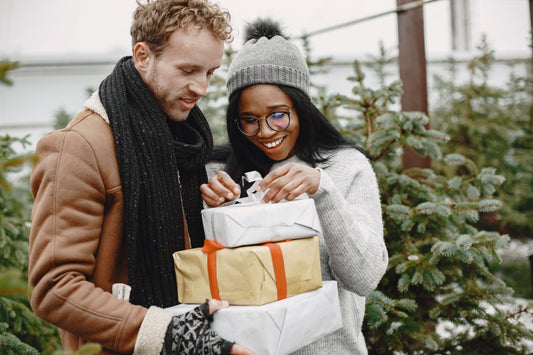 Smiling couple opening a stack of wrapped Christmas gifts at a Christmas tree farm