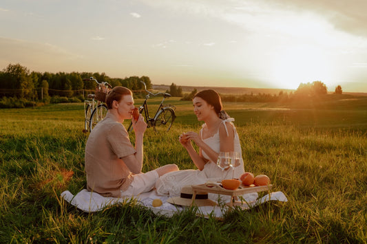 Couple sharing a picnic in a grassy field at sunset with bicycles behind them