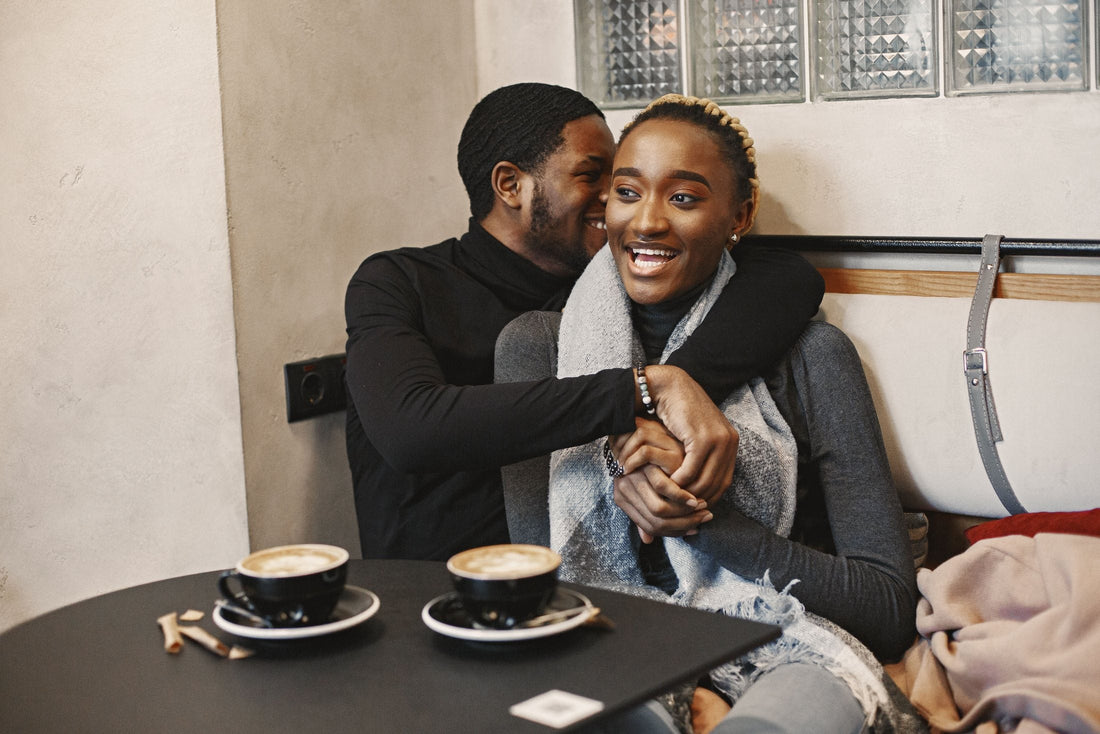 Smiling couple sharing a hug at a cafe table with two cups of coffee