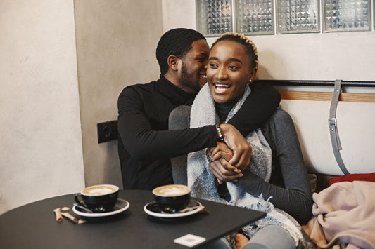 Smiling couple sharing a hug at a cafe table with two cups of coffee