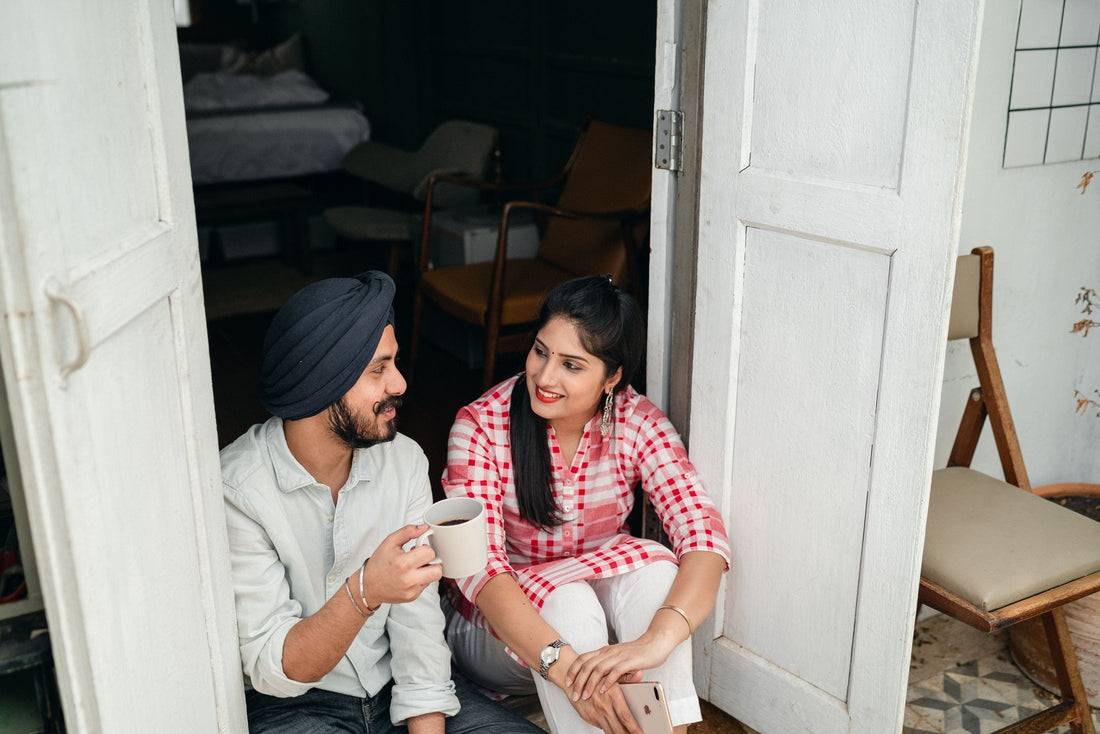 Couple sitting in an open doorway with morning coffee, talking and smiling