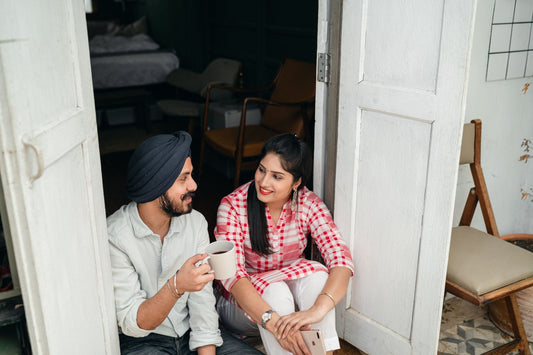 Couple sitting in an open doorway with morning coffee, talking and smiling