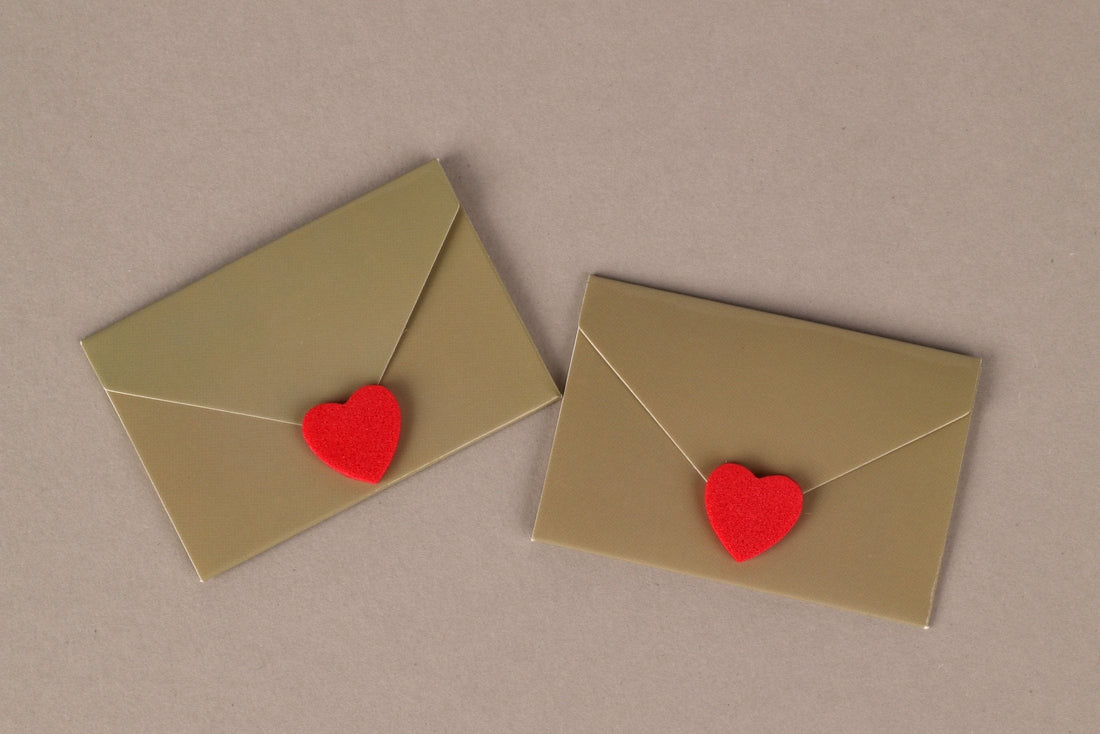 Two envelopes sealed with red heart stickers on a beige background