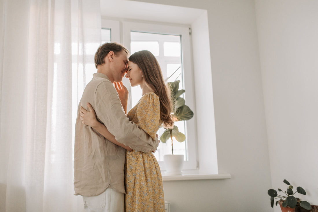 Couple embracing with foreheads touching by a bright window at home