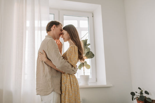 Couple embracing with foreheads touching by a bright window at home