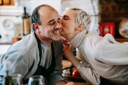 Woman kissing her partner on the cheek while he cooks in the kitchen