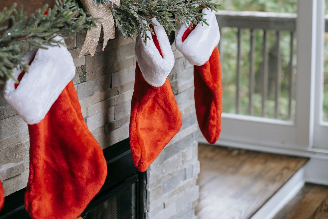 Red and white Christmas stockings hanging from a garland-trimmed mantel beside a bright window