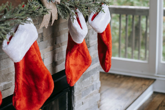 Red and white Christmas stockings hanging from a garland-trimmed mantel beside a bright window