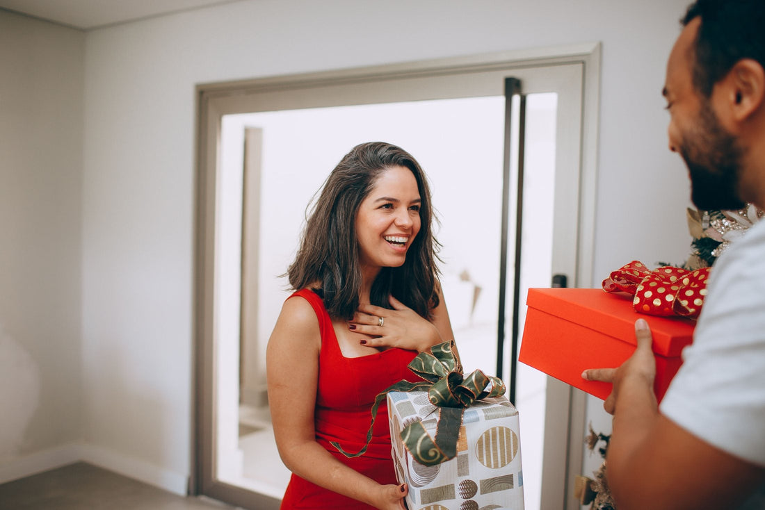 Woman in a red dress laughing as her husband hands her a wrapped gift