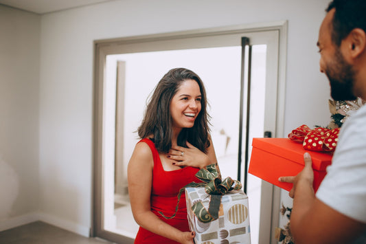 Woman in a red dress laughing as her husband hands her a wrapped gift