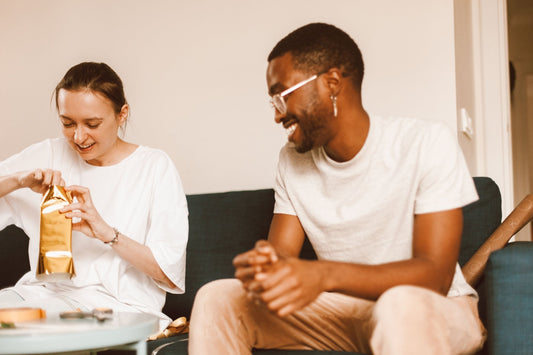 Couple laughing on a sofa as she unwraps a gift in gold paper