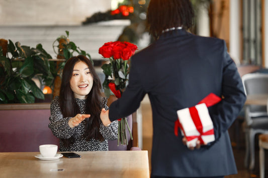 Woman delighted as her partner surprises her with red roses and a gift at a cafe